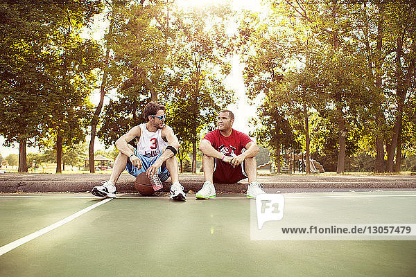 Freunde entspannen sich auf dem Basketballplatz gegen Bäume im Park