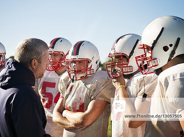 Trainer diskutiert mit American-Football-Spielern an einem sonnigen Tag