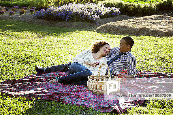 Happy couple drinking wine while lying on picnic blanket at grassy field