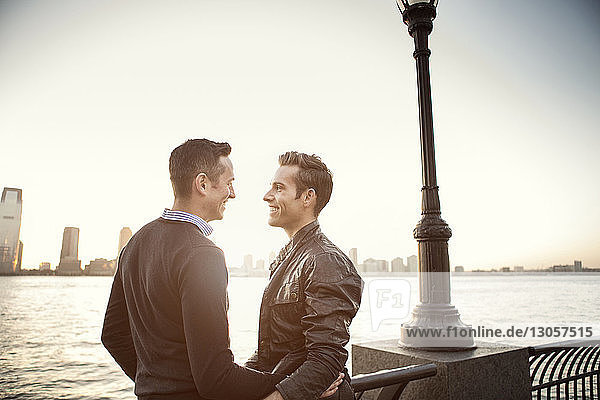 Glückliches homosexuelles Paar steht am Fluss gegen den Himmel