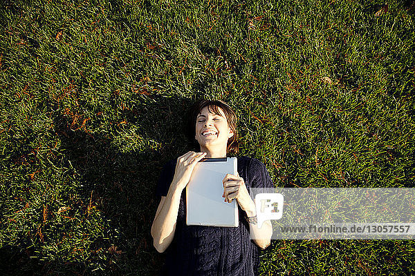 Draufsicht einer glücklichen Frau  die einen Tablet-Computer hält  während sie sich im Park entspannt