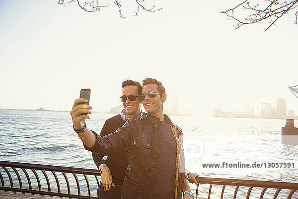 Homosexual couple taking selfie on mobile phone while standing by river