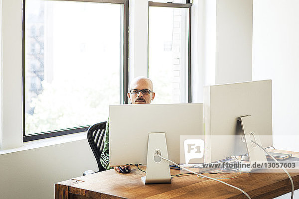 Businessman using computer while sitting against window in office
