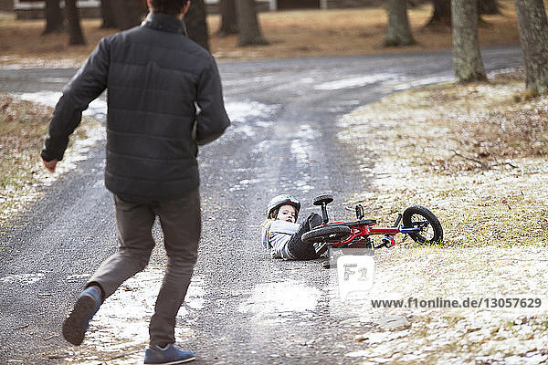 Rückansicht eines Vaters  der auf einen auf der Straße vom Fahrrad gefallenen Sohn zuläuft