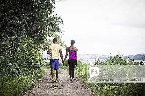 Rear view of couple holding hands while walking on road amidst grass