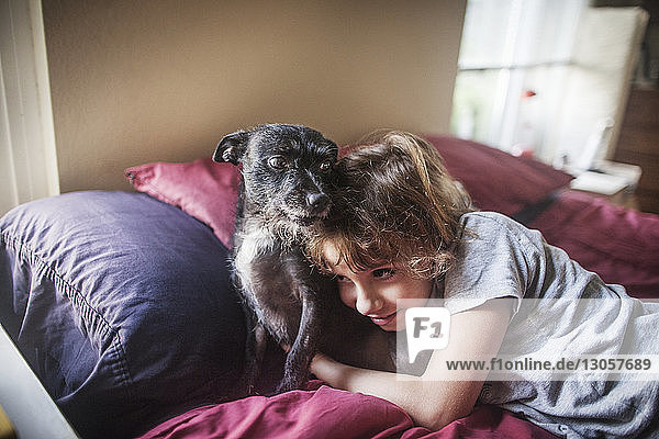 Girl embracing dog while lying on bed at home
