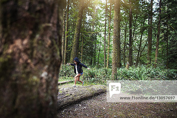 Playful girl running on fallen tree in forest