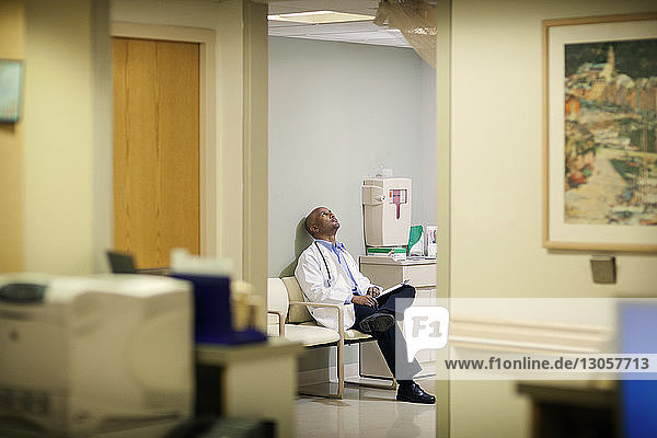 Arzt mit Bericht  der aufschaut  während er im Krankenhaus auf einem Stuhl sitzt
