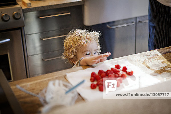 Cute boy looking at raspberries in kitchen