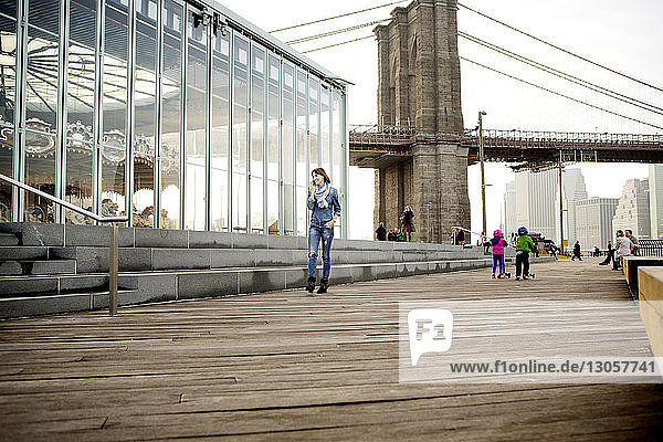 Frau telefoniert beim Vorbeigehen an Jane's Carousel gegen die Brooklyn Bridge