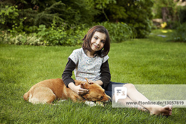 Portrait of girl sitting with dog on grassy field in yard