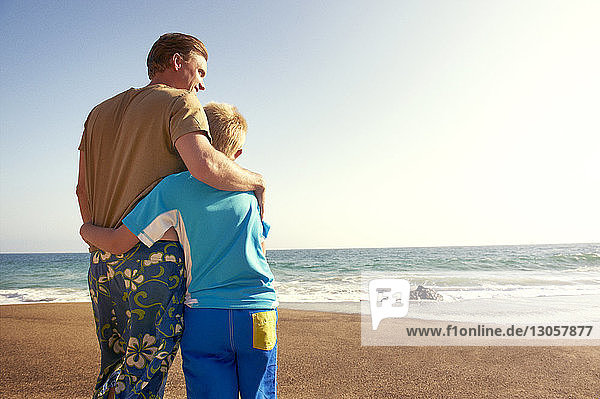 Father and son on sea shore at beach against clear sky