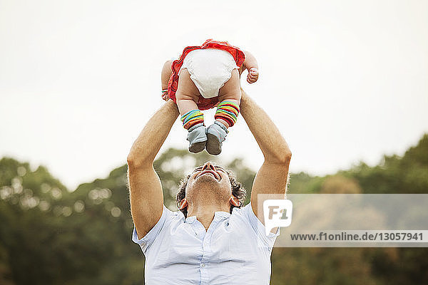 Father lifting baby girl while standing in park