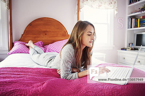 Junge Frau benutzt Laptop  während sie zu Hause auf dem Bett liegt
