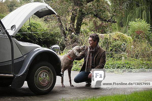 Man crouching while looking at dog by vintage car