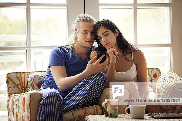 Ehepaar benutzt Mobiltelefon  während es zu Hause auf einem Sessel sitzt