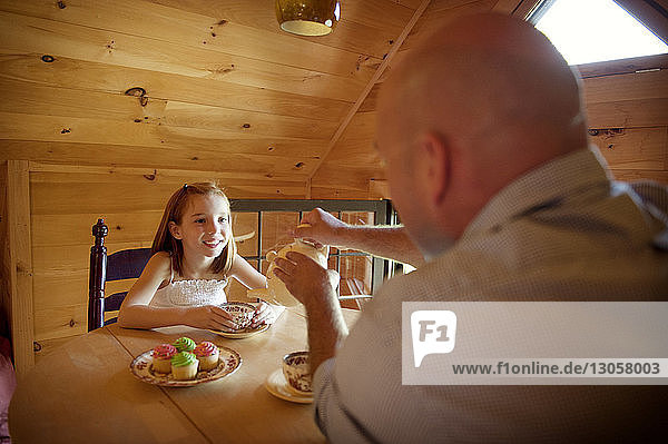Father serving tea to happy daughter while sitting at table
