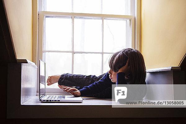 Junge benutzt Laptop-Computer  während er zu Hause auf dem Boden liegt