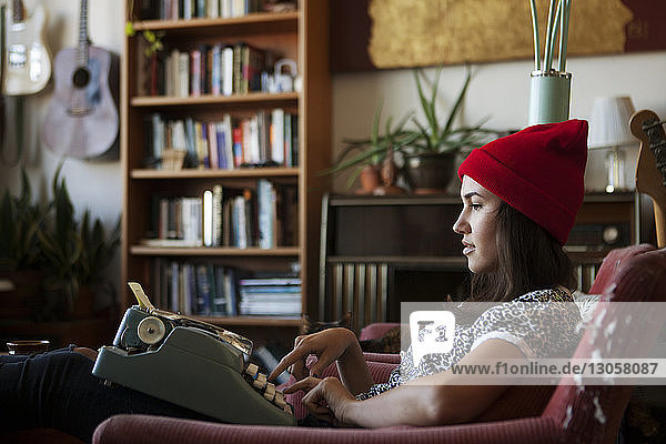 Seitenansicht einer Frau  die eine Schreibmaschine benutzt  während sie auf einem Stuhl sitzt