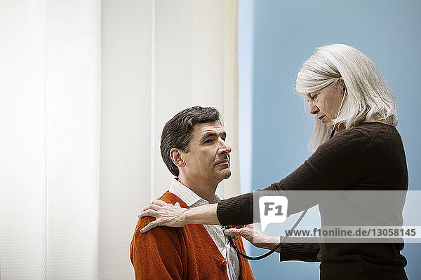 Doctor examining man with stethoscope in hospital