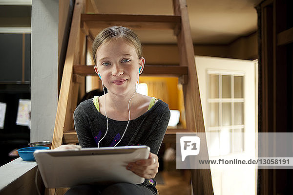Porträt eines Mädchens  das Musik hört  während sie zu Hause einen Tablet-Computer auf einer Leiter benutzt