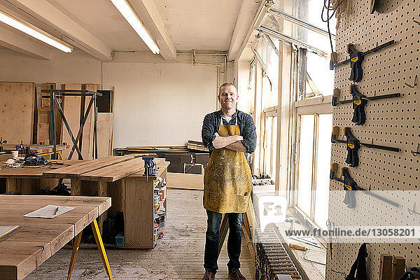 Portrait of male carpenter standing by windows in workshop