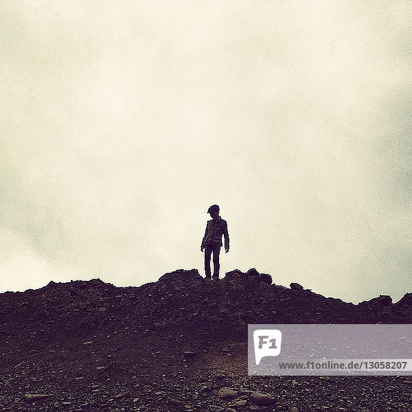 Low angle view of boy standing on mountain against sky
