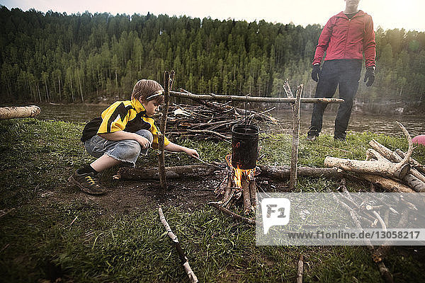 Boy preparing food on bonfire with father at campsite