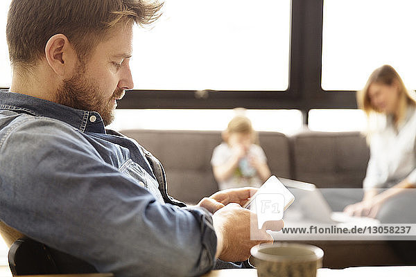 Man using tablet computer with family in background
