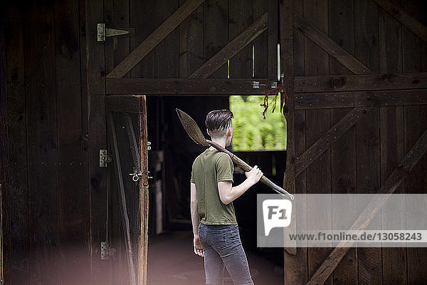 Jugendlicher Junge hält Schaufel  während er gegen eine Holzhütte steht