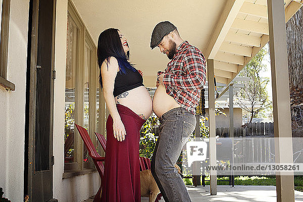 Seitenansicht eines Mannes  der auf der Veranda den Bauch einer schwangeren Frau berührt