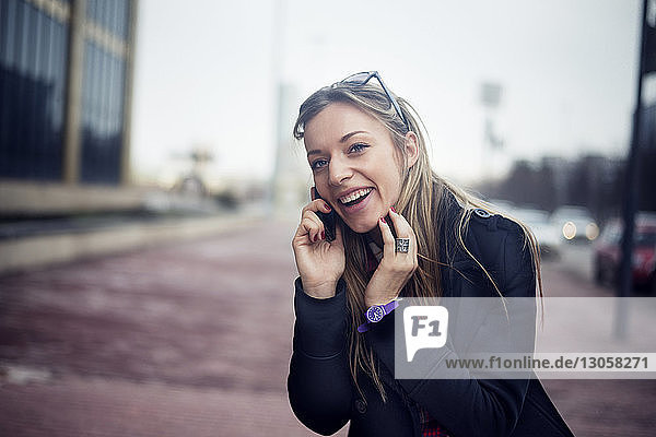 Happy young woman talking on phone in city