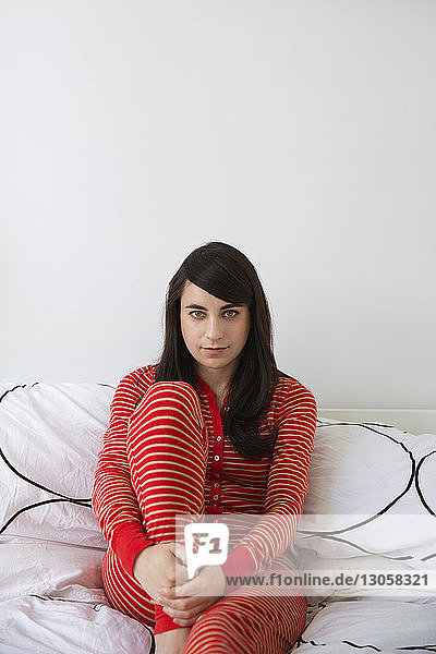 Porträt einer Frau  die zu Hause auf dem Bett an der Wand sitzt
