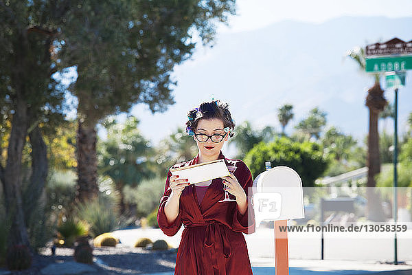 Frau  die Post liest  während sie am Briefkasten steht