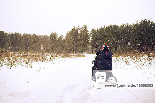 Rückansicht eines Jungen  der auf einem schneebedeckten Feld Schlitten fährt