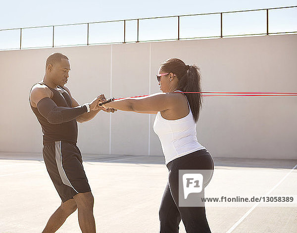 Trainer hilft Sportlerin beim Seilziehen an sonnigem Tag