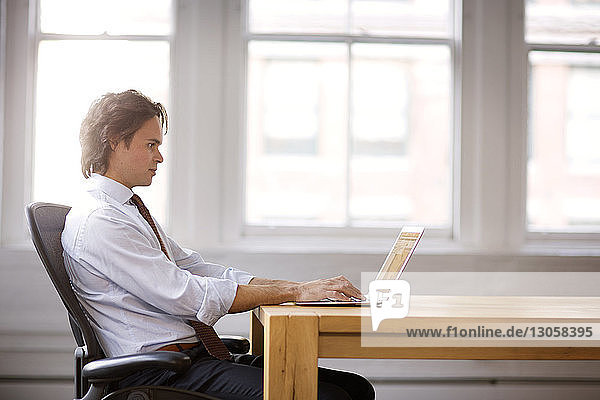 Seitenansicht eines am Laptop arbeitenden Geschäftsmannes am Tisch im Büro