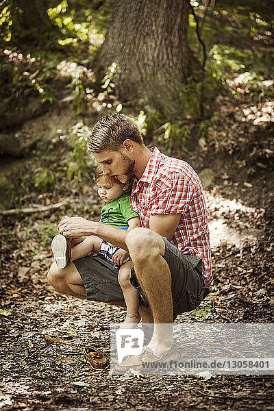 Vater bindet dem Sohn die Schnürsenkel  während er auf einem Feld im Wald kauert