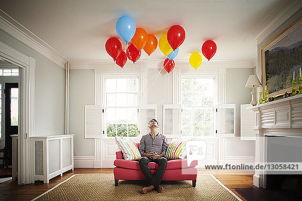 Mann schaut zu Hause auf Luftballons  während er auf dem Sofa sitzt