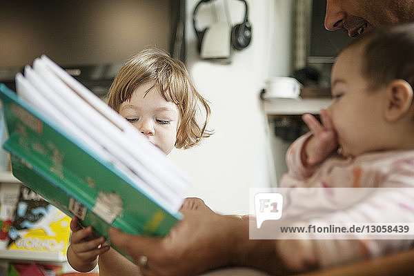 Ausgeschnittenes Bild eines Vaters  der ein Buch hält  während er mit seinen Töchtern zu Hause sitzt