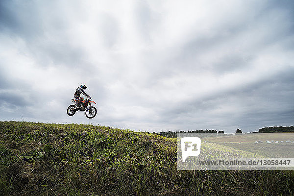 Biker führt Stunt auf Hügel gegen bewölkten Himmel aus