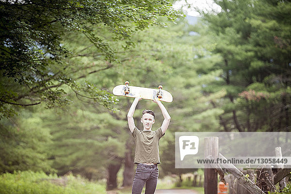 Porträt eines Teenagers  der ein Skateboard hält  während er an Bäumen steht