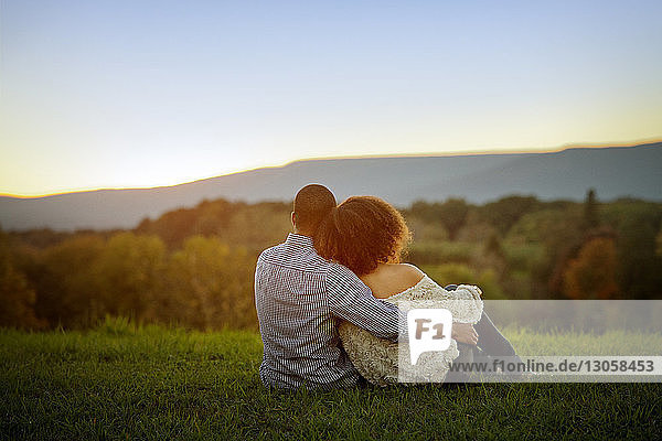 Rear view of couple sitting on grassy field during sunset