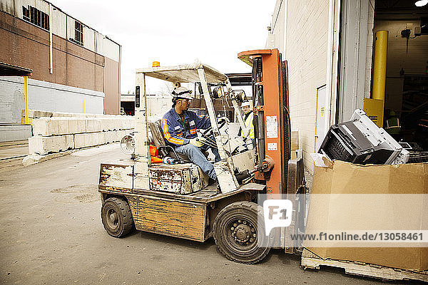 Arbeiter bewegt Kiste mit Gabelstapler im Recyclingwerk