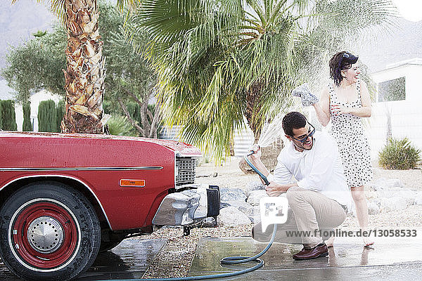 Mann besprüht Frau beim Autowaschen auf Parkplatz mit Wasser