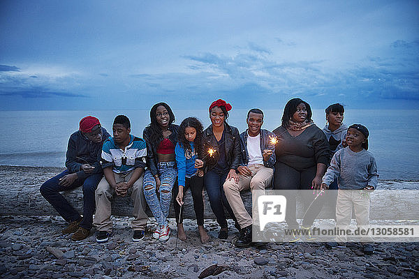 Familie und Freunde sitzen auf einem Baumstamm am Strand gegen den Himmel