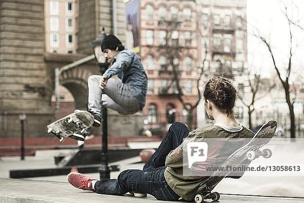Man relaxing while friend skateboarding at skateboard park