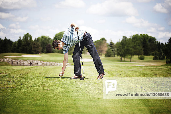 Full length of man placing ball on tee at golf course