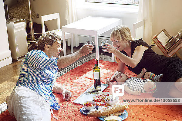 Familie genießt Essen und Trinken  während sie zu Hause auf dem Teppich liegt