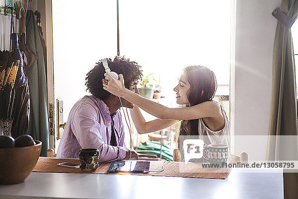 Frau hilft Mann beim Tragen eines Kopfhörers bei Tisch zu Hause